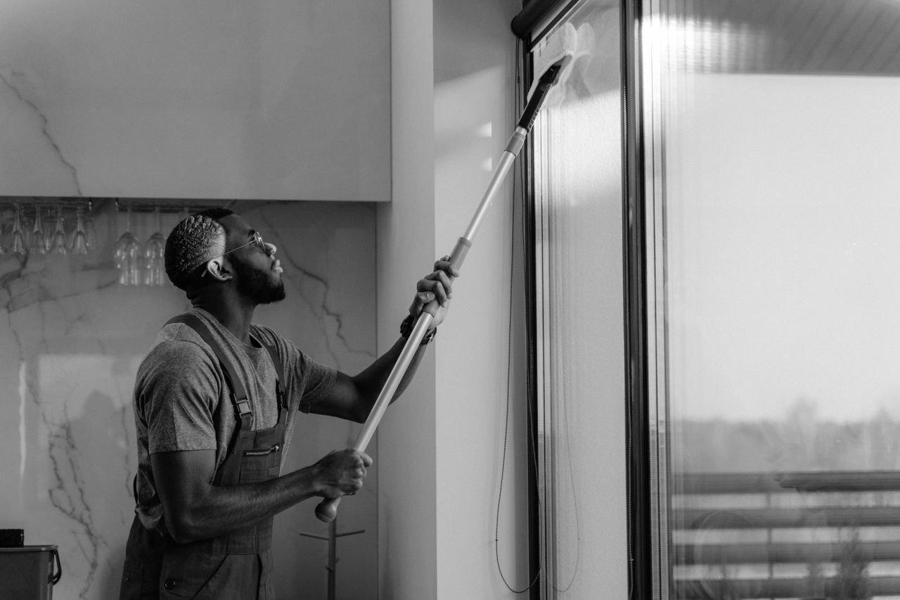 about-002 A man cleaning a glass window with a mop in grayscale, showcasing professional work.
